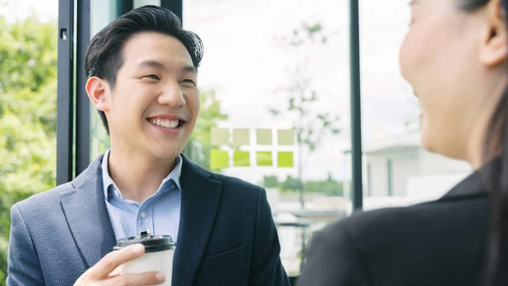 Close-up of a happy Asian man in a suit jacket looking at a woman during a casual conversation.