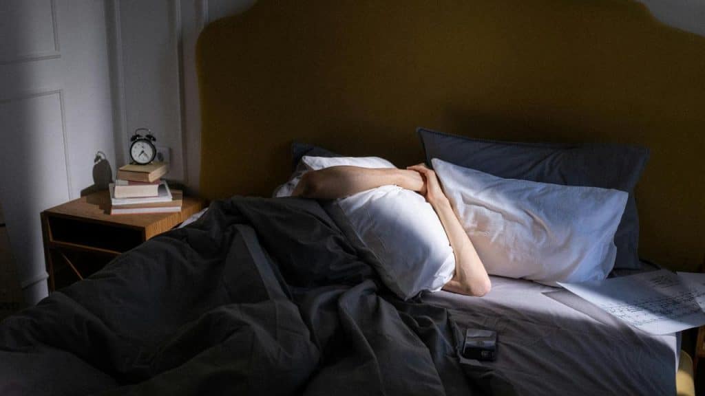 A person lying in bed with a pillow over their head.