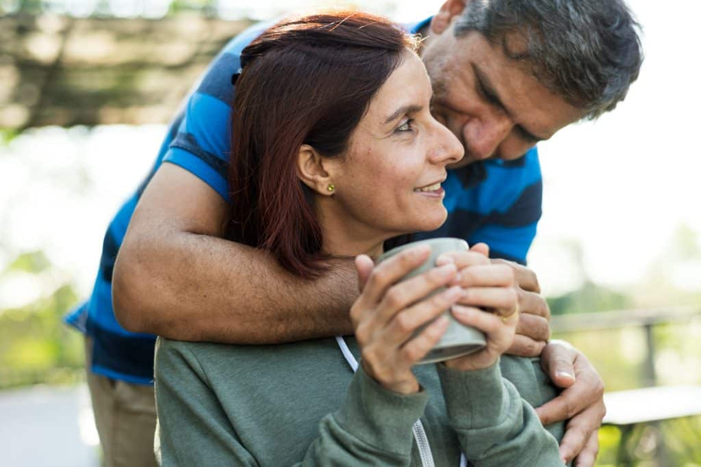 The man is hugging the woman holding the cup.