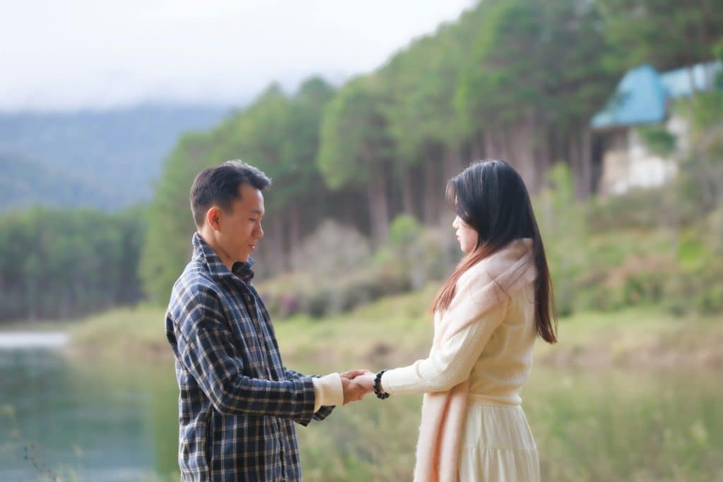 The man and the woman are holding hands beside the lake.