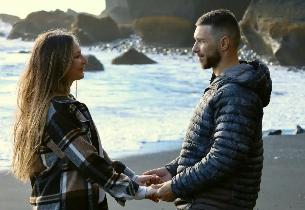 The couple is holding each other’s hands at the beach.