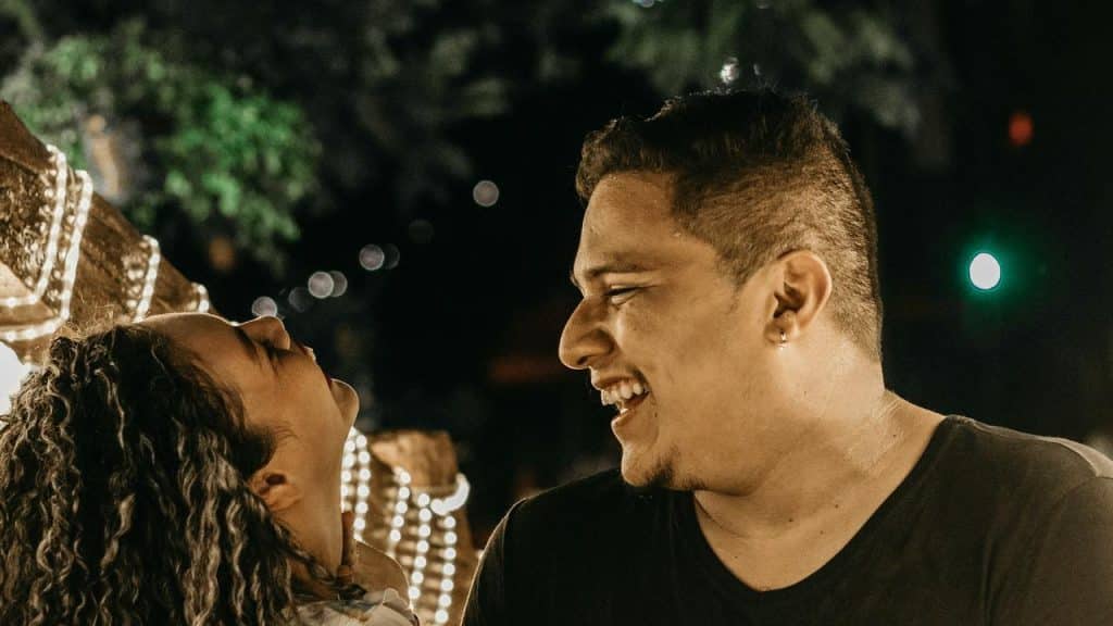 A couple laughing together at night under string lights.