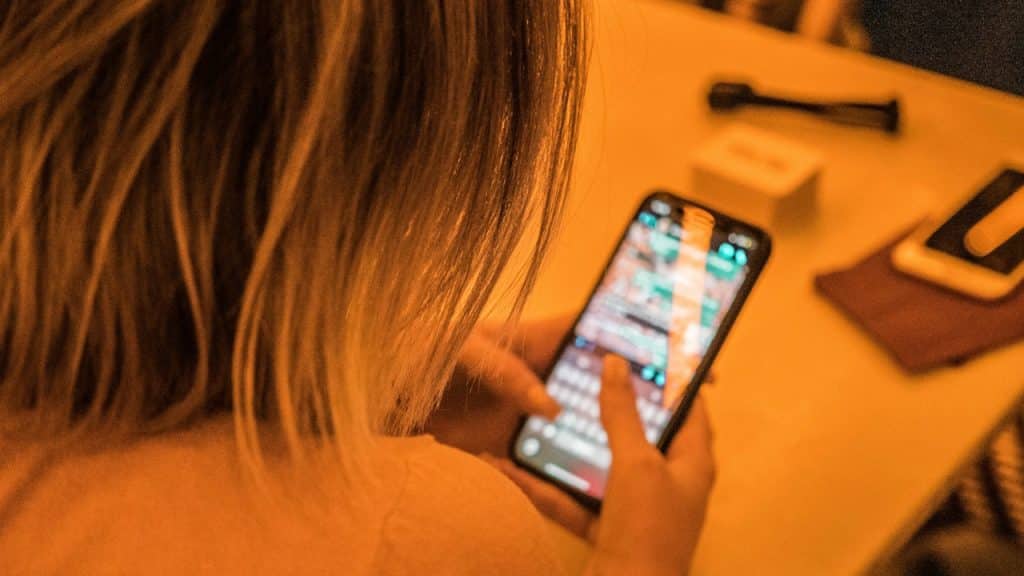 Over-the-shoulder view of a person with blonde hair looking at and typing on a smartphone at a table.