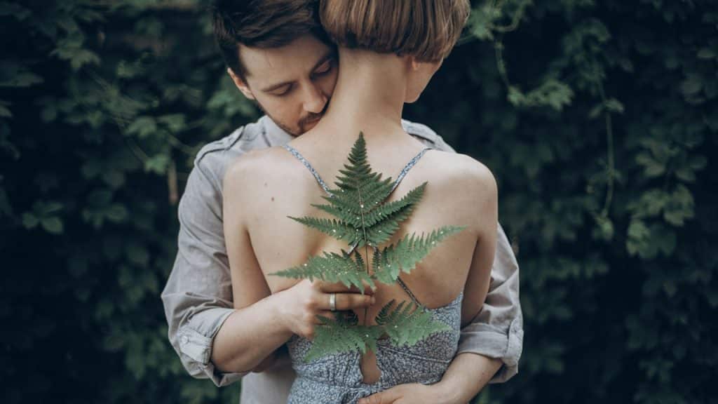 A man and woman embracing in green leaves.