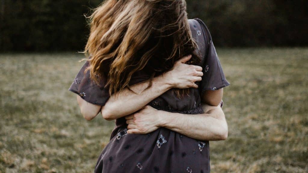 Two people embracing outdoors in a grassy field.