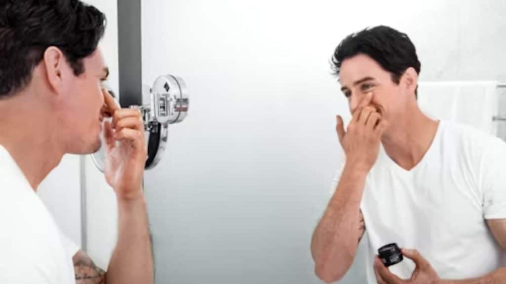 Man applying moisturizer in front of a bathroom mirror