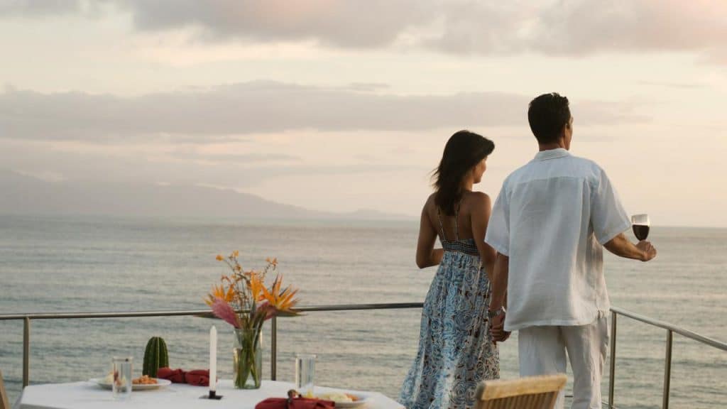 A couple holding hands and enjoying an ocean view at sunset.
