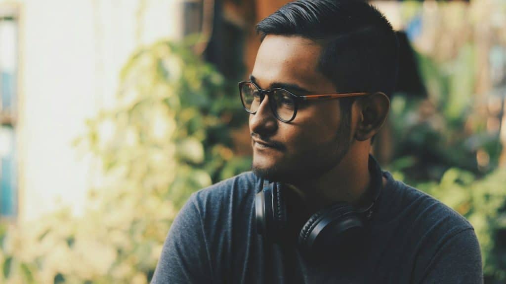 Man in glasses with headphones around his neck, looking off to the side, outdoors.