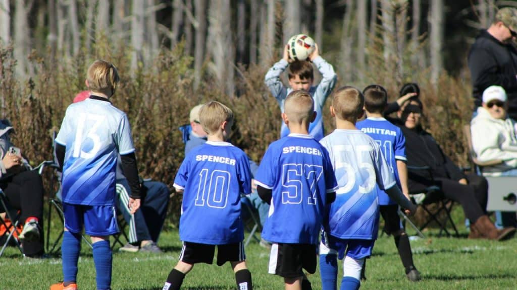 Young boys in blue soccer jerseys are playing with a ball on a sunny field.