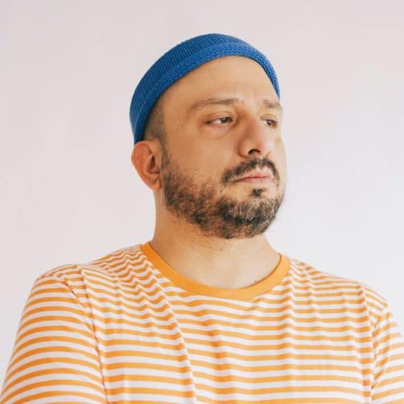 Man in a blue knit cap and orange striped shirt looking away from the camera.