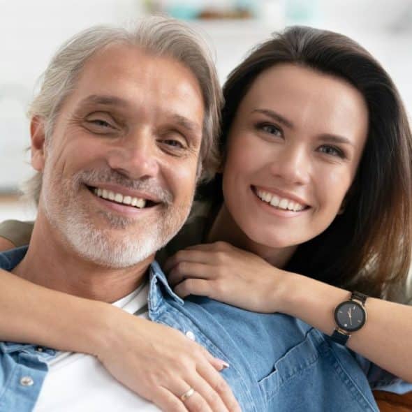 A happy, smiling older man and younger woman in a close-up, affectionate embrace.