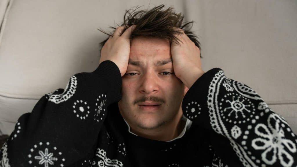 Man lying down, holding his head with both hands, looking stressed or overwhelmed.