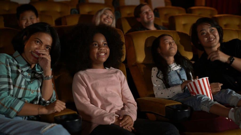 Diverse group of people smiling and watching a movie in a darkened theater.