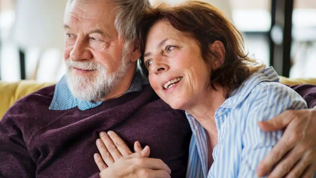 Senior man and woman embracing on a couch, looking off to the side.