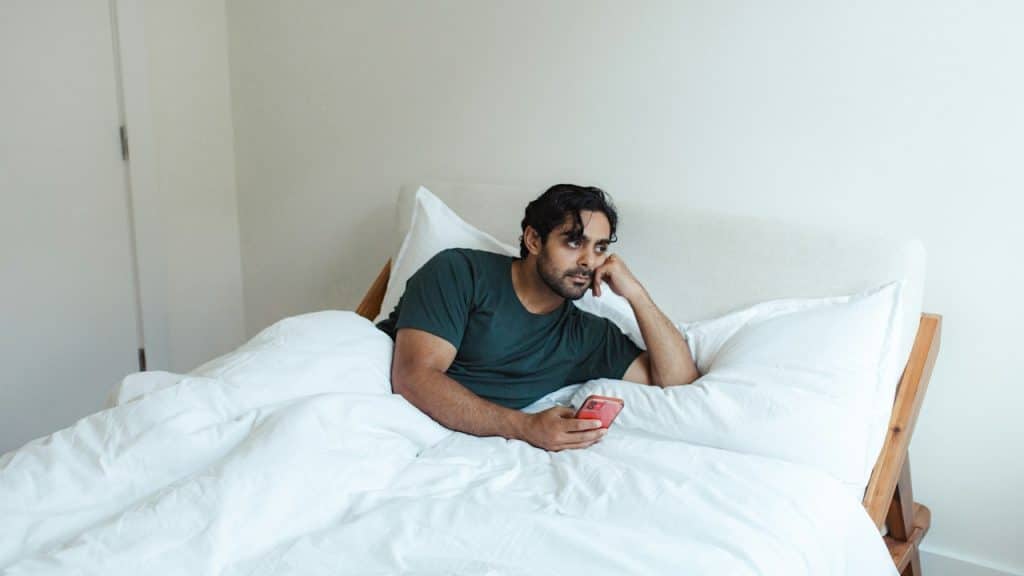 A man in a green t-shirt in bed holding a phone.