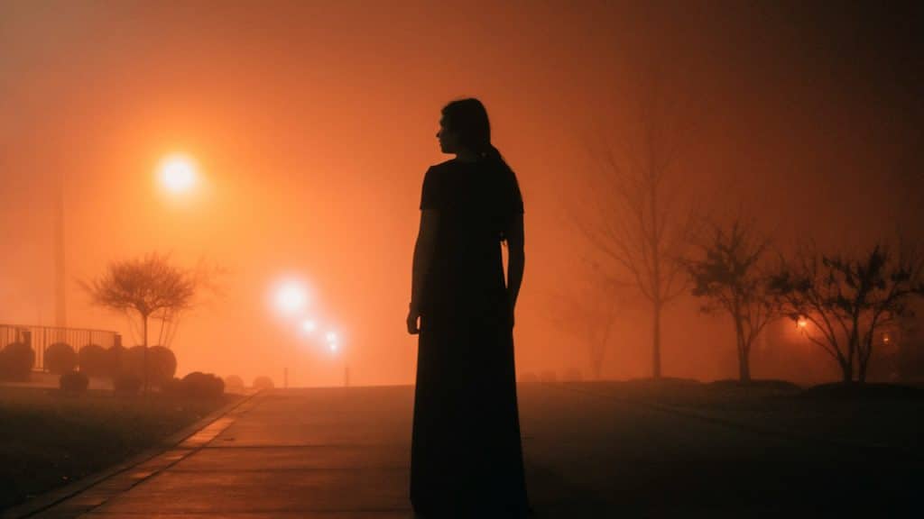 Silhouette of a woman standing on a road in a foggy night. 