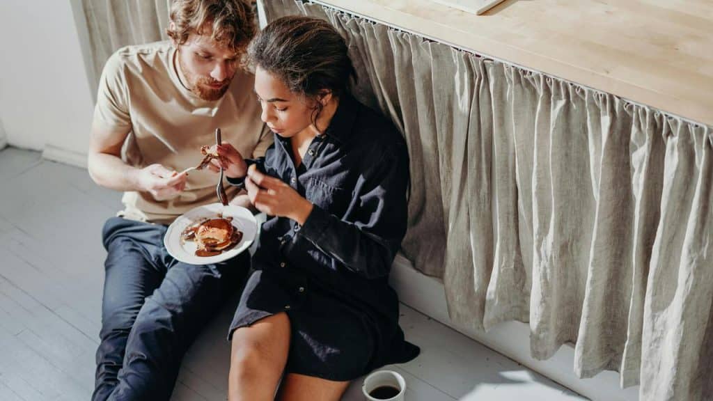 A couple sitting on the floor sharing pancakes and coffee.