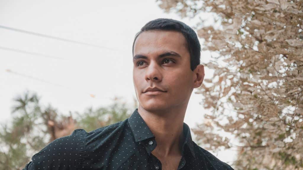 A young man standing in front of a tree.