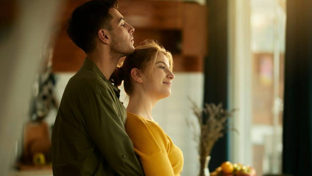 A man holding a woman while she gazes out of a window. 