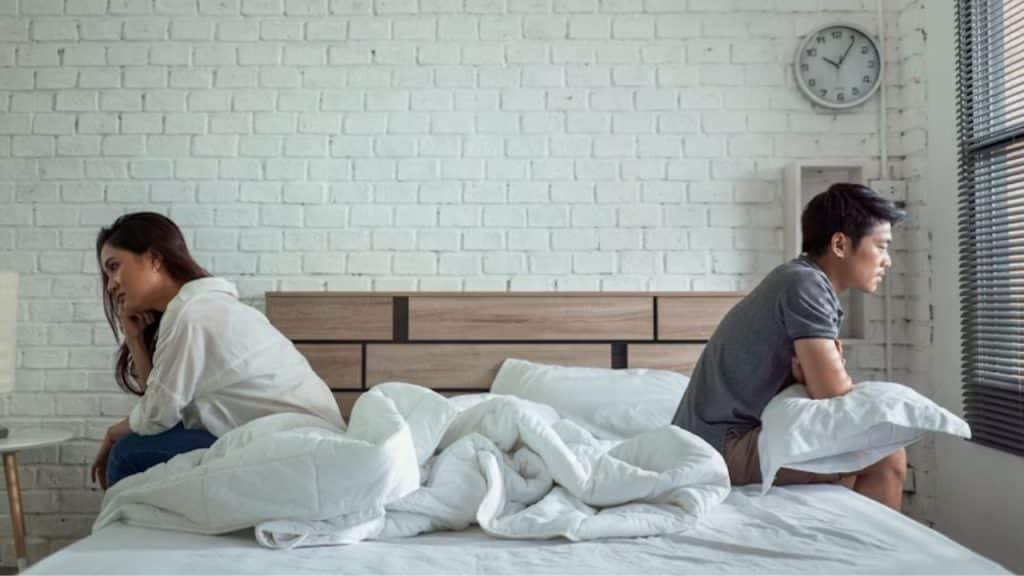 Couple sitting apart in bed, both looking away