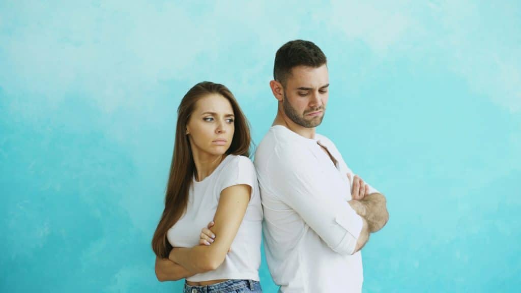 A couple with crossed arms standing with their backs to each other.