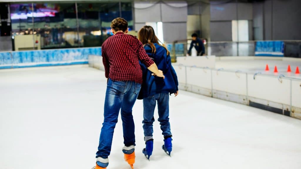 A man supporting his partner while skating at an indoor skating rink.