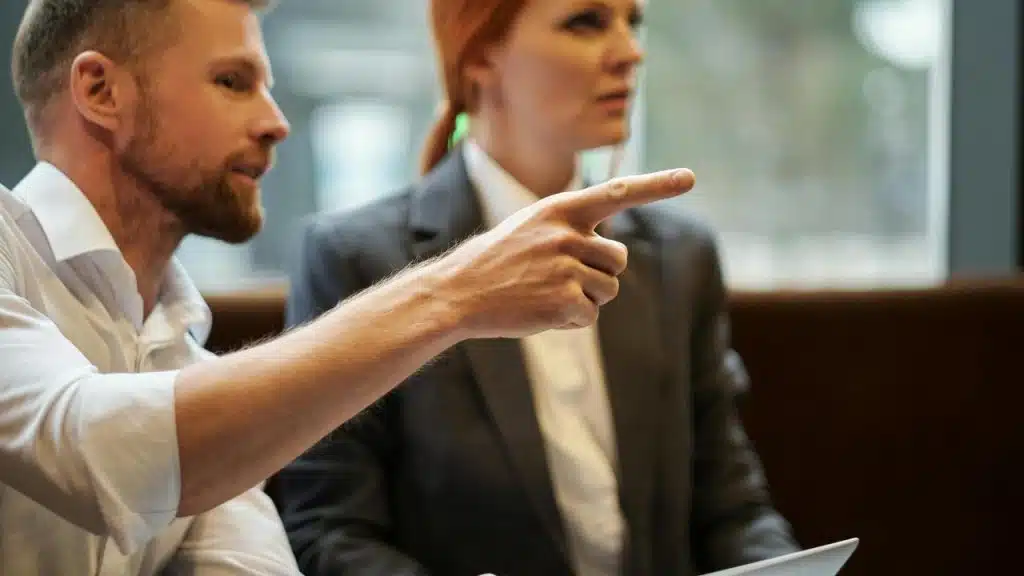 A man pointing while talking to a woman in a meeting.