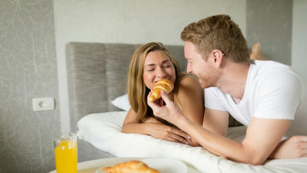 A happy couple enjoying breakfast in their bed.