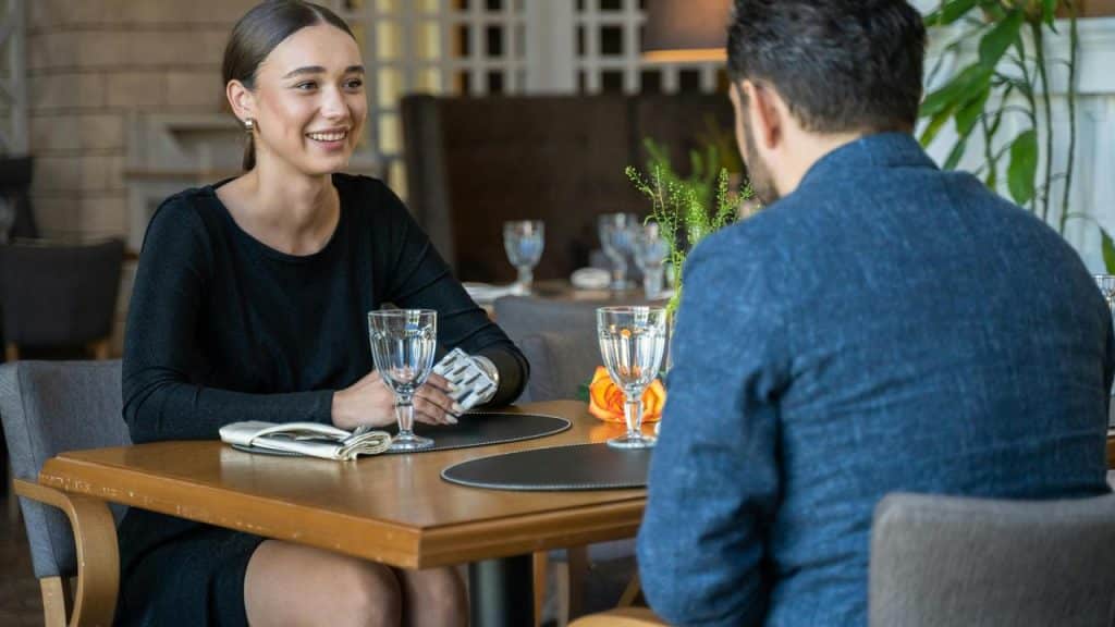 A woman smiling while talking to a man at a restaurant table.