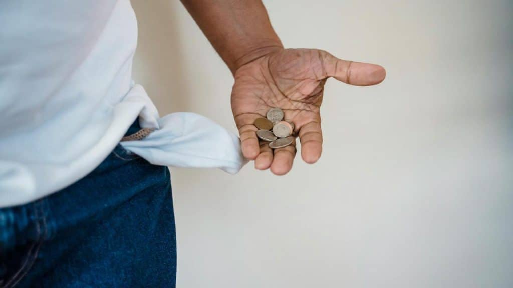 A person holding a few coins with an empty pocket turned inside out.