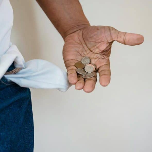 A person holding a few coins with an empty pocket turned inside out.