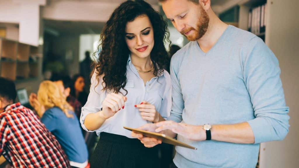 A man and woman looking at a tablet and discussing something in an office.