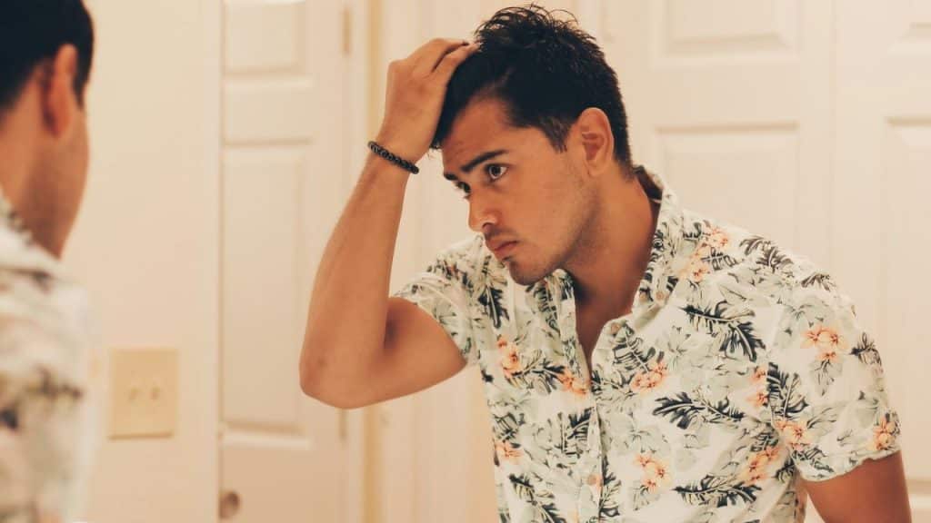 Young man in a floral shirt looking at his reflection and adjusting his hair.