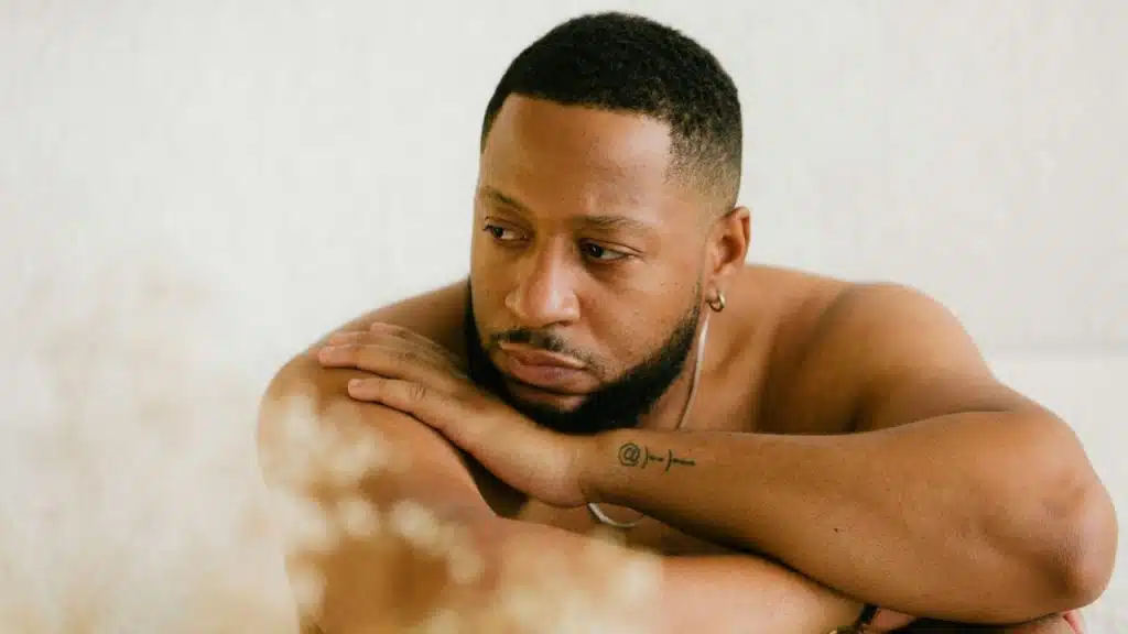 Man with a beard and tattoo, looking away, resting his head on his arms.