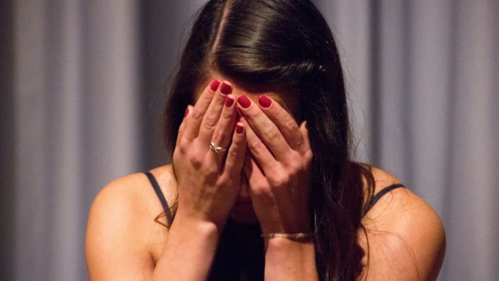 Woman with red nail polish covering her face with her hands, wearing a ring.