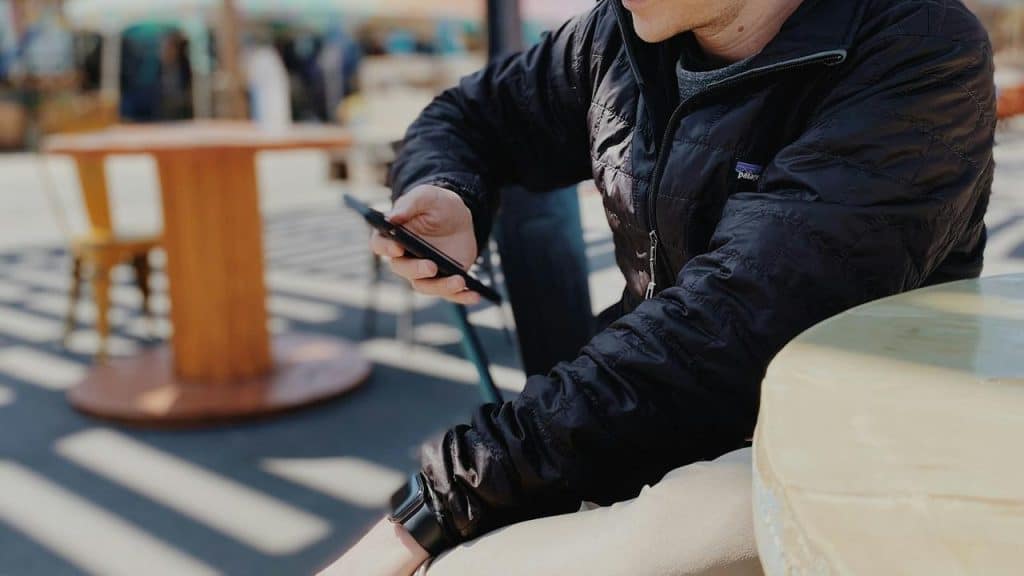 A person sitting at an outdoor café using a smartphone.