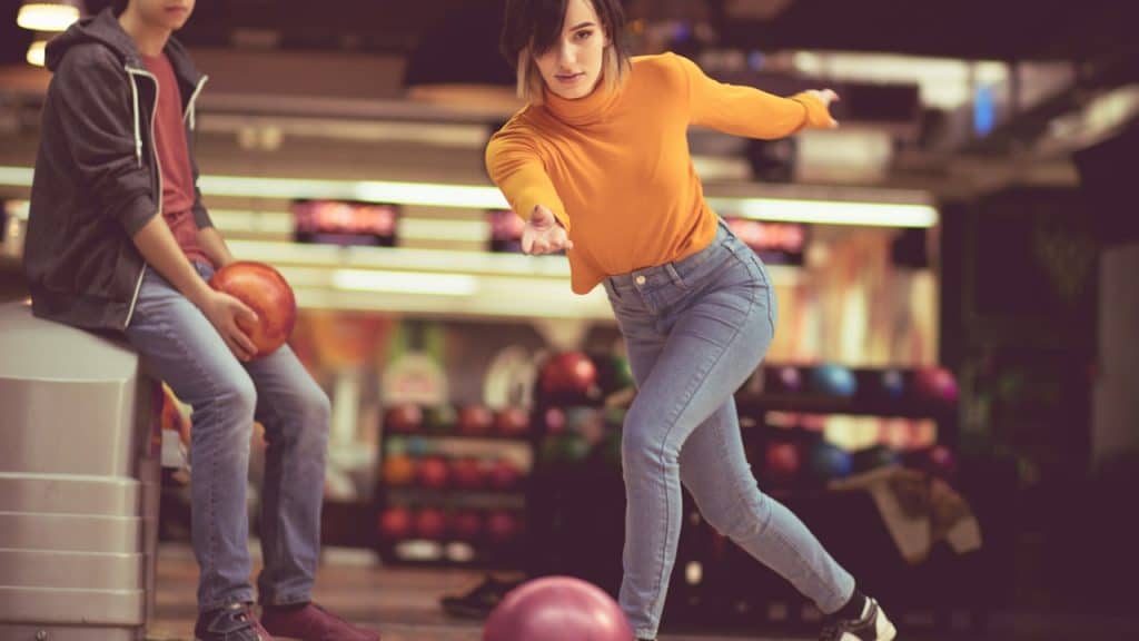 A couple in a bowling alley where the woman is throwing a bowling ball.