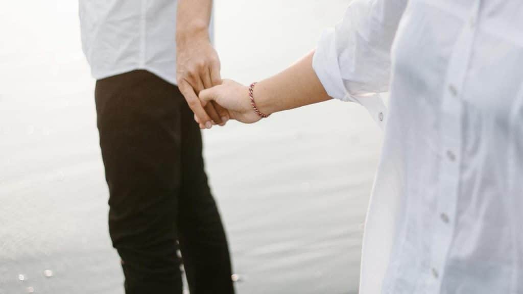 A man and woman holding hands while standing near water.