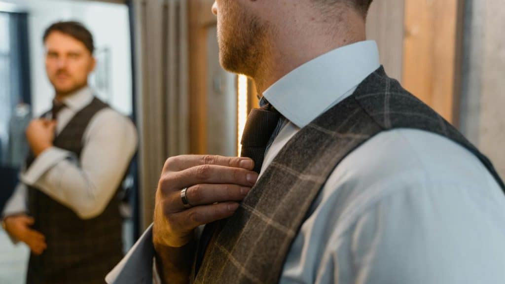 A man adjusting his tie while looking at himself in a mirror.