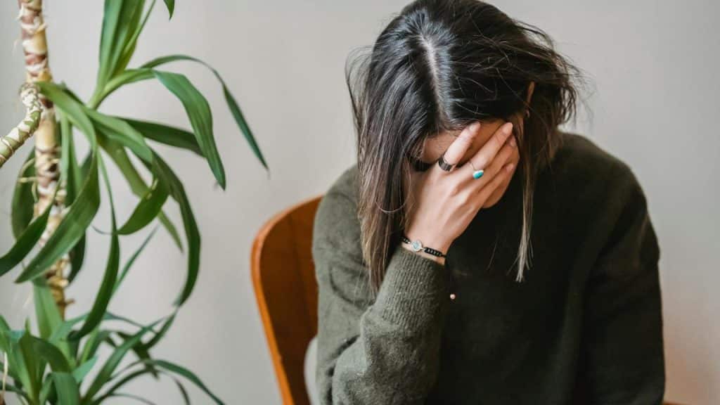 A woman sitting with her hand covering her face, appearing stressed or upset.