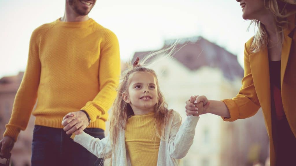 A couple with their daughter wearing the same color dresses and holding hands.