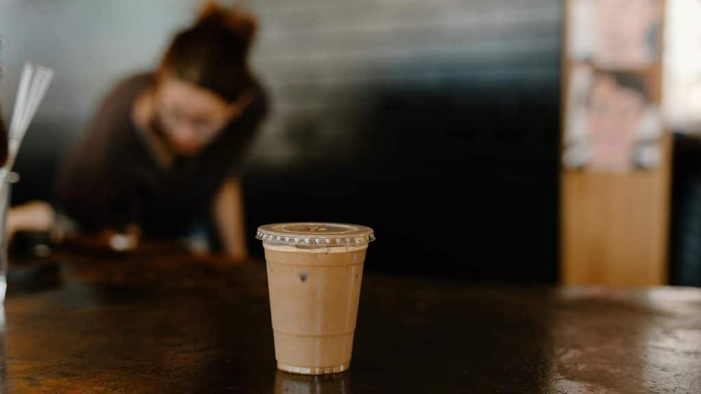 A cup of iced coffee on a counter with a barista in the background.
