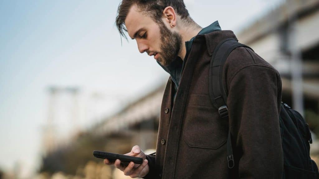 A person standing outdoors looking down at a smartphone.