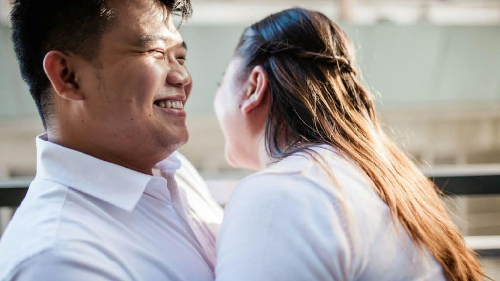 Close-up of a smiling man in a white shirt looking at a woman with long brown hair.