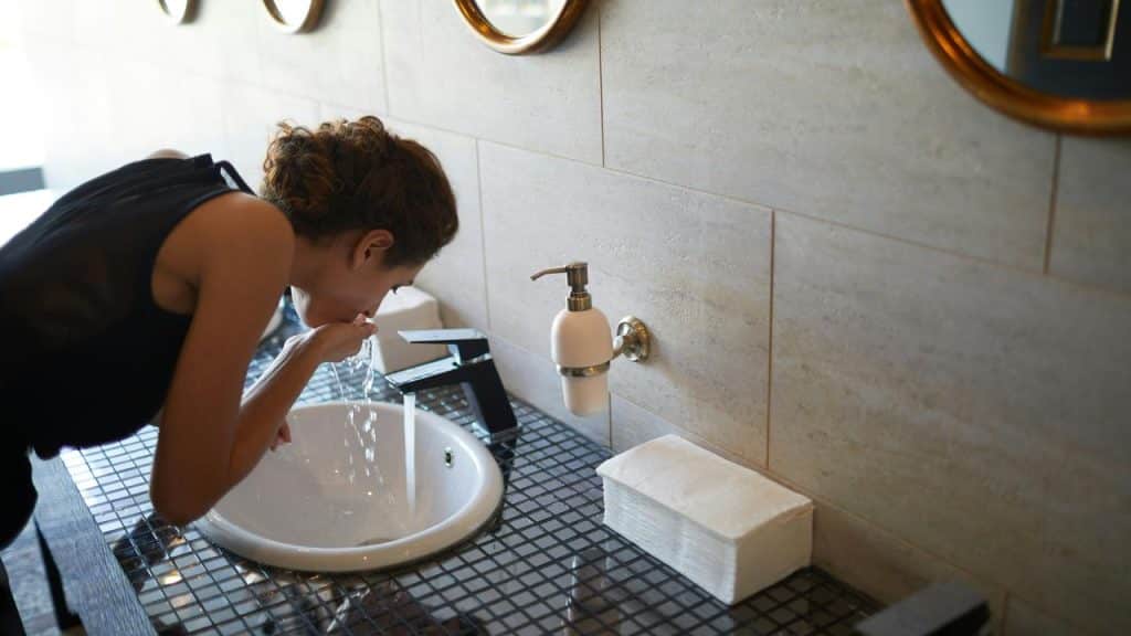 A woman leaning over a sink splashing water on her face.