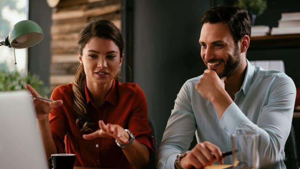 A man and a woman working on a laptop and discussing with each other.