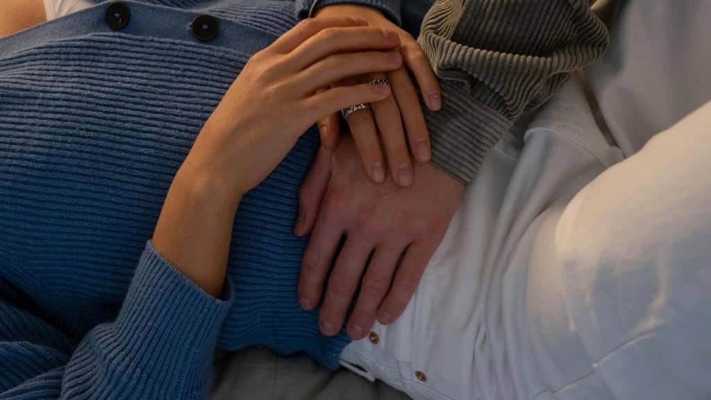 A close-up of two people lying together with their hands gently resting on each other.