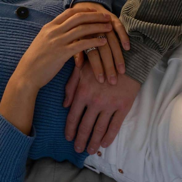 A close-up of two people lying together with their hands gently resting on each other.