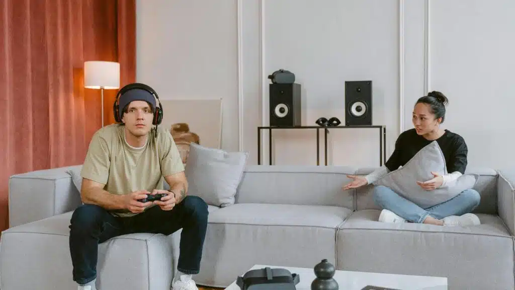 A man gaming while a woman speaks to him on the couch.
