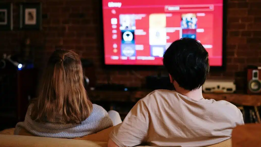 A couple sitting on a couch watching a TV screen.